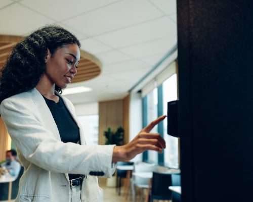 Close up view of woman's finger pushing number button on keyboard of snack vending machine. Self-used technology and consumption concept